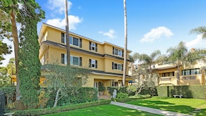 A two-story yellow building with a well-maintained lawn, a stone bench, and a pathway leading to the entrance.