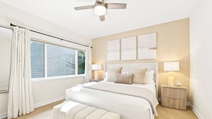 A bedroom with a bed, bedside tables, a ceiling fan, and a window with curtains.