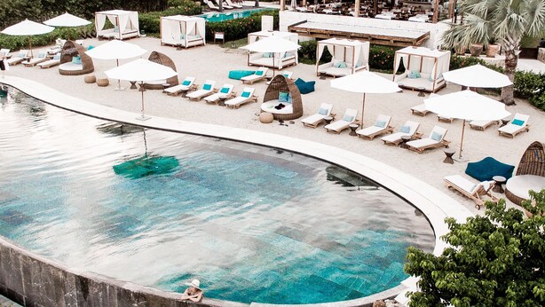 Ein Poolbereich mit Liegestühlen und Sonnenschirmen, umgeben von Grünflächen und einem Gebäude im Hintergrund.