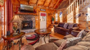 A cozy log cabin interior with a fireplace, leather sofa, and wooden walls.