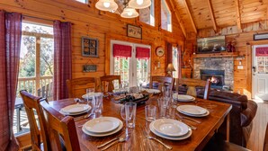 A wooden cabin interior with a dining table set for four, a fireplace, and a stone wall.