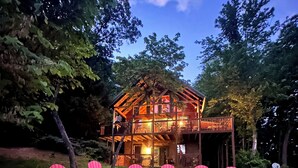 A wooden cabin with a porch and multiple red Adirondack chairs arranged around a fire pit.