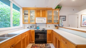 A modern kitchen with wooden cabinets, a microwave, a stove, and a window providing a view of greenery.