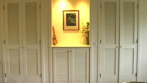 A room with white shutters, a framed picture, and a guitar on a shelf.