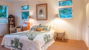 A bedroom with a bed, a bookshelf, a chair, a bedside table, and two windows.