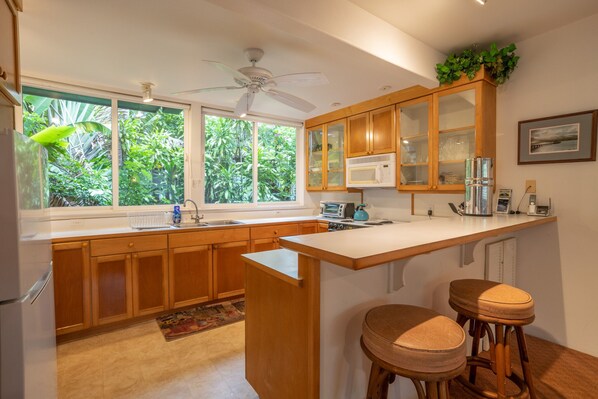 A kitchen with wooden cabinets, a white countertop, a built-in microwave, and a ceiling fan.