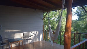 Una terraza de madera con una hamaca, sillas y vistas a un follaje exuberante.