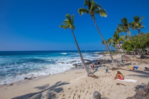 A beach with palm trees, ocean waves, and people relaxing. - Oceanfront Condo, 5G Wi-Fi, King Bed, Hot Tub/Pool, Free Parking (Kailua-Kona)