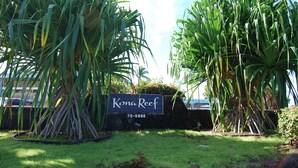 A sign for Kona Reef with a stone wall and large tropical plants. - Oceanfront Condo, 5G Wi-Fi, King Bed, Hot Tub/Pool, Free Parking (Kailua-Kona)