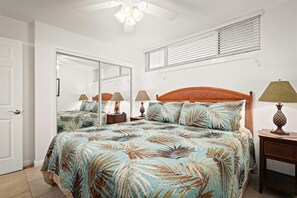 A bedroom with a bed, two nightstands, a ceiling fan, a window with blinds, and a door. - Oceanfront Condo, 5G Wi-Fi, King Bed, Hot Tub/Pool, Free Parking (Kailua-Kona)