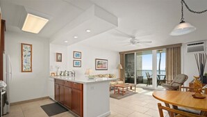 A modern kitchen with a central island, a dining area with a round table, and a balcony with a view. - Oceanfront Condo, 5G Wi-Fi, King Bed, Hot Tub/Pool, Free Parking (Kailua-Kona)