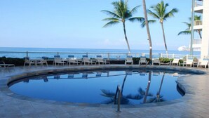 A pool with lounge chairs and palm trees, overlooking the ocean. - Oceanfront Condo, 5G Wi-Fi, King Bed, Hot Tub/Pool, Free Parking (Kailua-Kona)