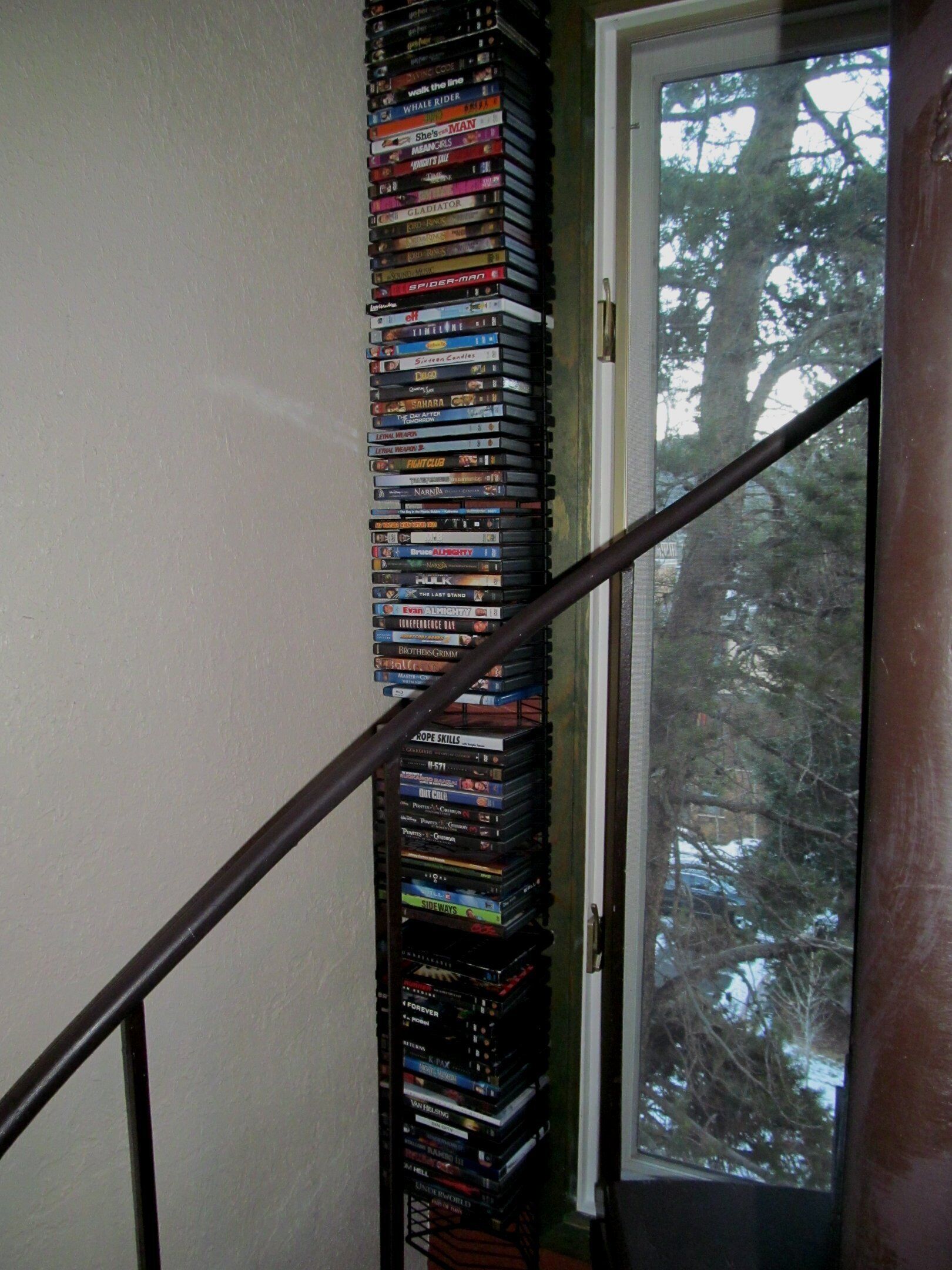 A staircase with a collection of DVDs stacked against the wall, leading to a door with a view of trees outside.