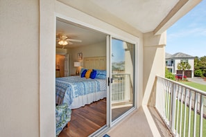 A bedroom with a bed, a ceiling fan, and a sliding glass door leading to a balcony.