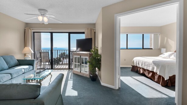 A hotel room with a balcony, a bed, a sofa, a TV, and a desk.