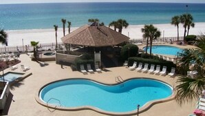 A beachside resort with a large swimming pool, lounge chairs, and a gazebo overlooking the ocean.