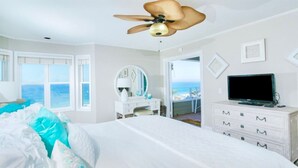 Un dormitorio con cama, televisor, cómoda, espejo y ventilador de techo.