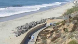 Un paseo marítimo costero con un camino curvo, afloramientos rocosos y una playa con olas.