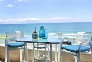 Enjoy the ocean view from this balcony with a table and two chairs.