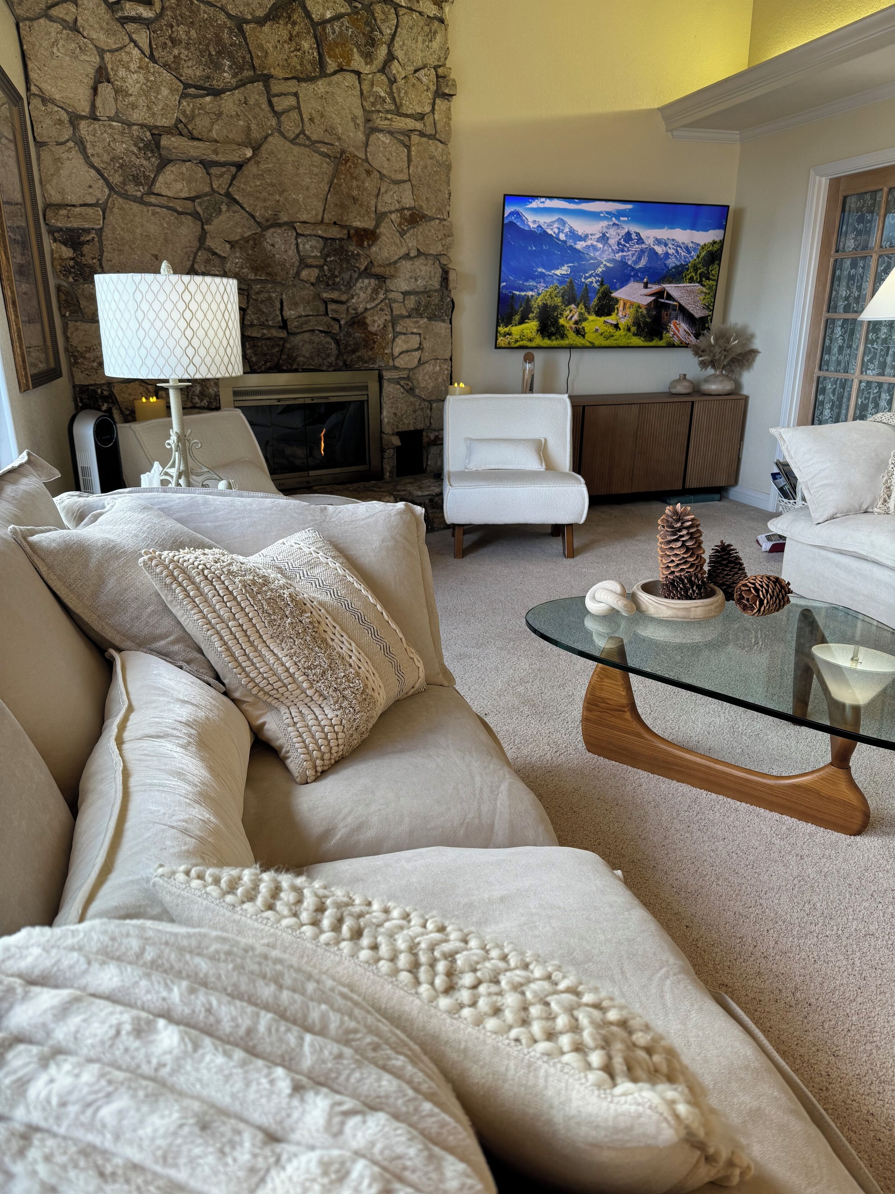 A living room with a stone wall, a fireplace, a television, a white sofa, and a glass coffee table.
