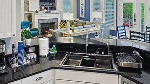 Ett modernt kök med en dubbel diskho, vita köksluckor och en matplats med en soffa och en tv.