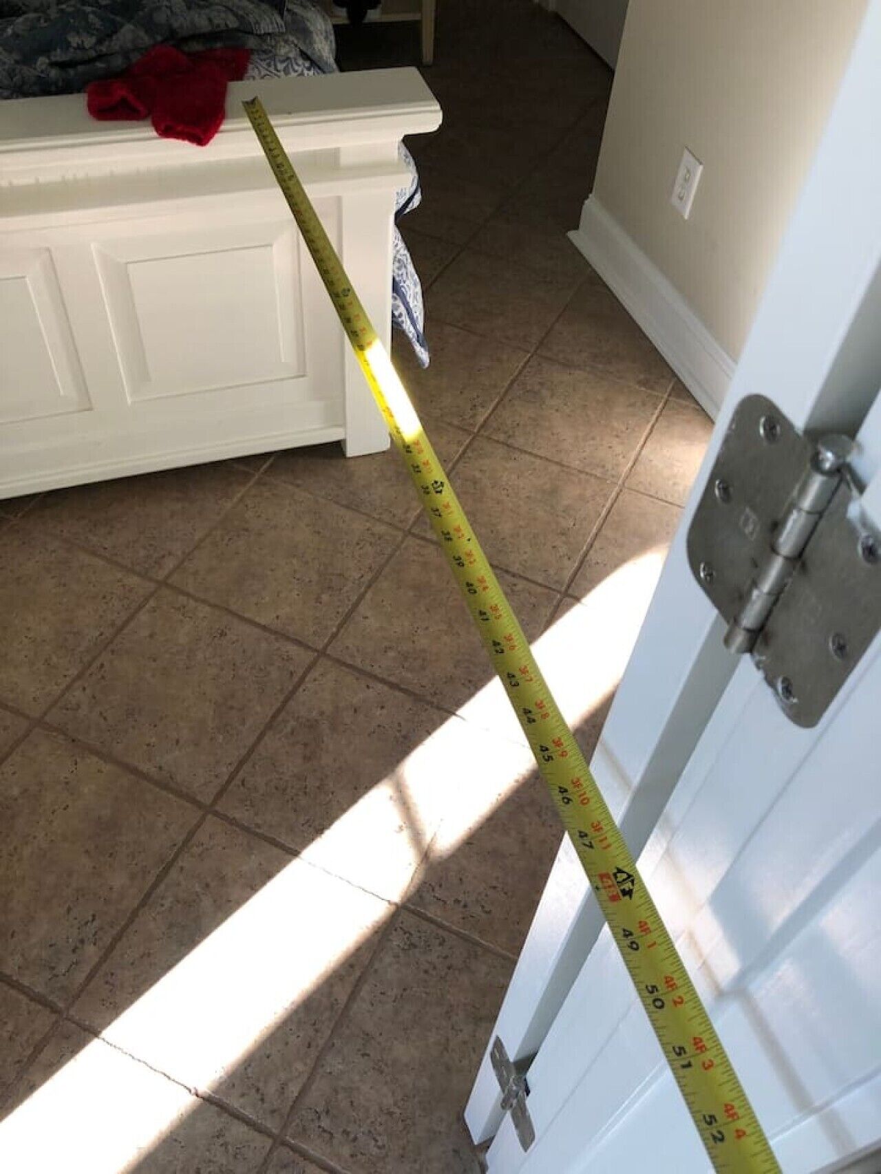 A measuring tape against a white door, a red cloth on a white piece of furniture, and a tiled floor.