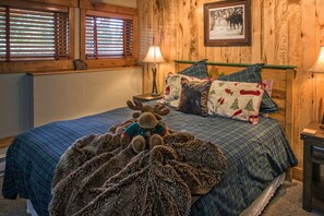 Une chambre confortable avec une couvre-lit à carreaux, un coussin orné d’un motif d’élan et une lampe sur une table de chevet.