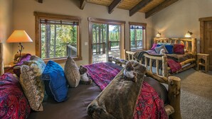 A cozy cabin room with a large bed, a smaller sofa, and a wooden headboard. There are two windows providing views of the forest. - SmallGroup-SmallRate! Great Layout/Views/HotTub/PoolTable/Grills/Ski In Ski Out! (Breckenridge)