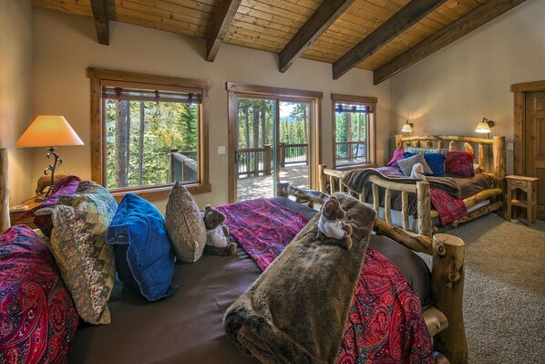 Ein gemütliches Cabin-Zimmer mit einem großen Bett, einer kleinen Couch und einem Holzkopfende. Zwei Fenster bieten Blick auf den Wald.