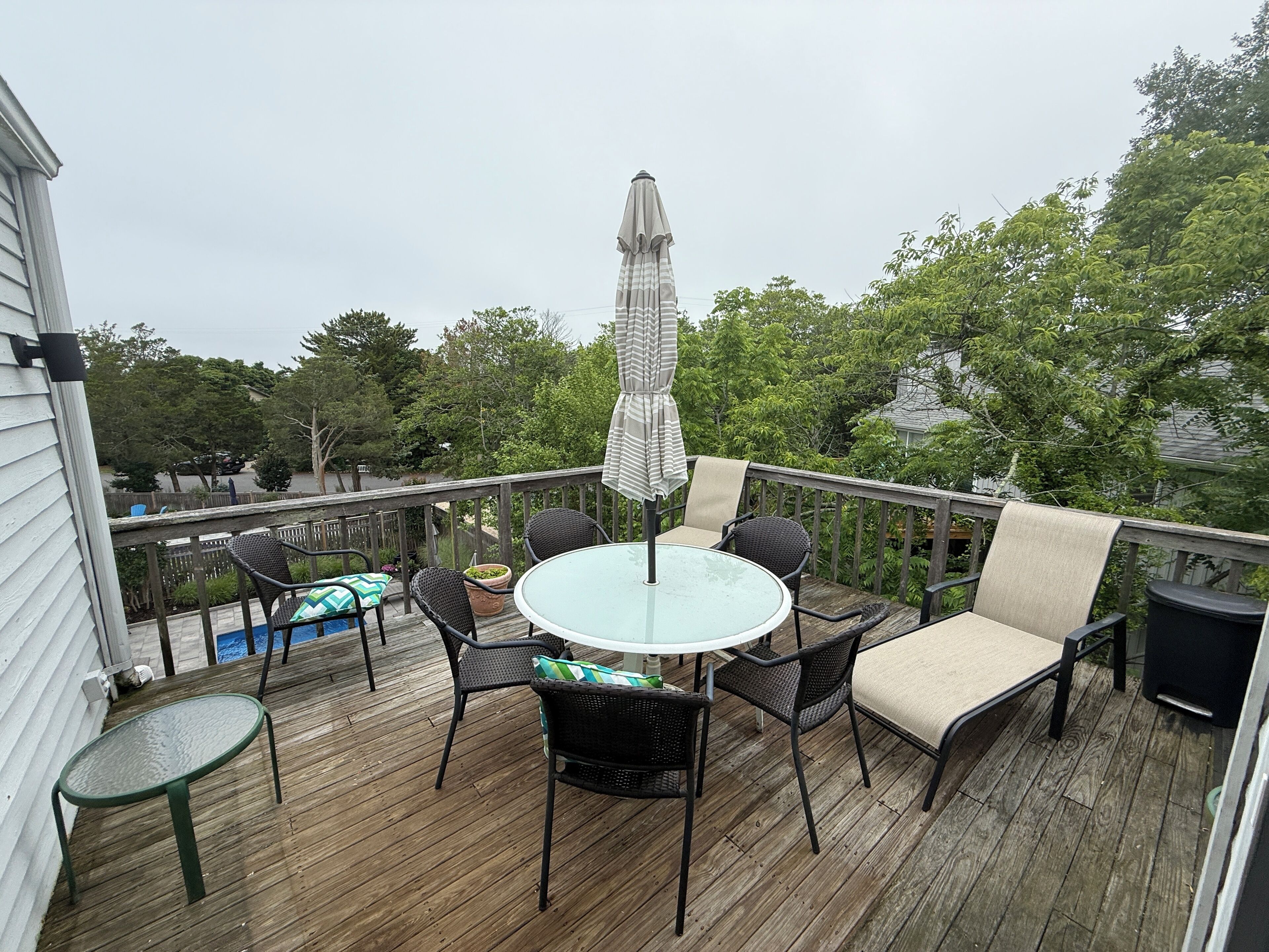 A wooden deck with a glass table and chairs, surrounded by a railing.