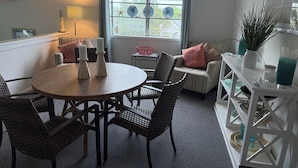 A cozy living room with a round wooden table, wicker chairs, a striped sofa, and a window with decorative plates. - Stunning 3BR, 2BA penthouse 5 blocks from lighthouse. Last week open 8/16-23! (Barnegat Light)