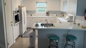 A modern kitchen with white cabinets, a built-in oven, a sink, and two bar stools. - Stunning 3BR, 2BA penthouse 5 blocks from lighthouse. Last week open 8/16-23! (Barnegat Light)