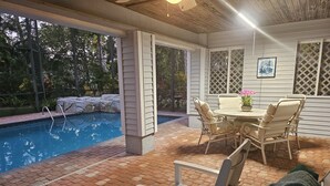 A covered outdoor area with a pool, patio furniture, and a view of the surrounding greenery.