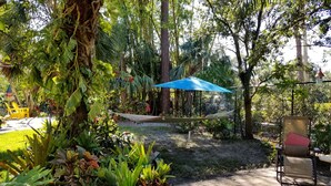 A garden with a hammock, a blue umbrella, and a chair.