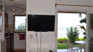 A kitchen with a TV mounted on the wall, a dining area with a table and chairs, and a view of the ocean through the window. - Beautiful Ocean/Beachfront Property and A Private Back Yard!  AC in both BDRMS! (Kailua-Kona)