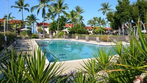 A swimming pool surrounded by palm trees and lounge chairs, with buildings in the background. - Beautiful Ocean/Beachfront Property and A Private Back Yard!  AC in both BDRMS! (Kailua-Kona)