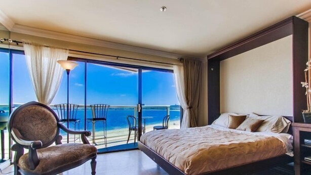 A bedroom with a large bed, a chair, and a balcony with a view of the sea. - Bayfront - Mission Bay on Sand Panoramic View -Upscale (San Diego)