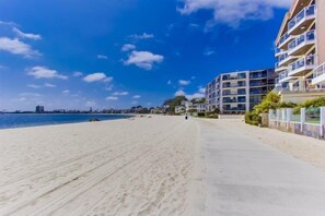 A beach with a concrete walkway, a building with multiple balconies, and a clear blue sky.