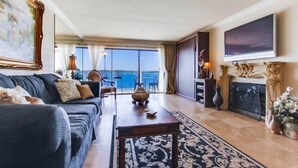 A spacious living room with a large sofa, a coffee table, and a fireplace. There is a large window with a view of the ocean. - Bayfront - Mission Bay on Sand Panoramic View -Upscale (San Diego)