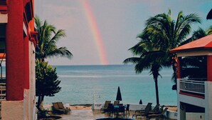 Uitzicht op het strand met ligbedden, palmbomen en een zichtbare regenboog.