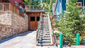 Una escalera de madera que conduce a un edificio con una pared de piedra a la izquierda y un árbol a la derecha.