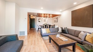 Una sala de estar moderna con piso de madera, un conjunto de sofá, una mesa de centro y un comedor con una mesa y sillas.