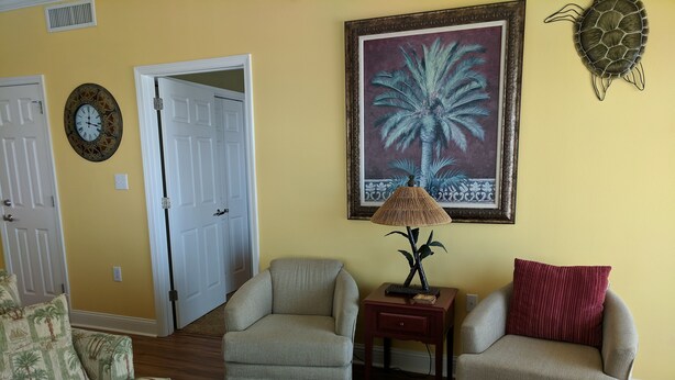 A living room with two armchairs, a coffee table, a lamp, a painting, and a door. - Gulf Beachfront: Beautiful Luxury West Corner Unit, Wrap-Around Balcony! (Gulf Shores)