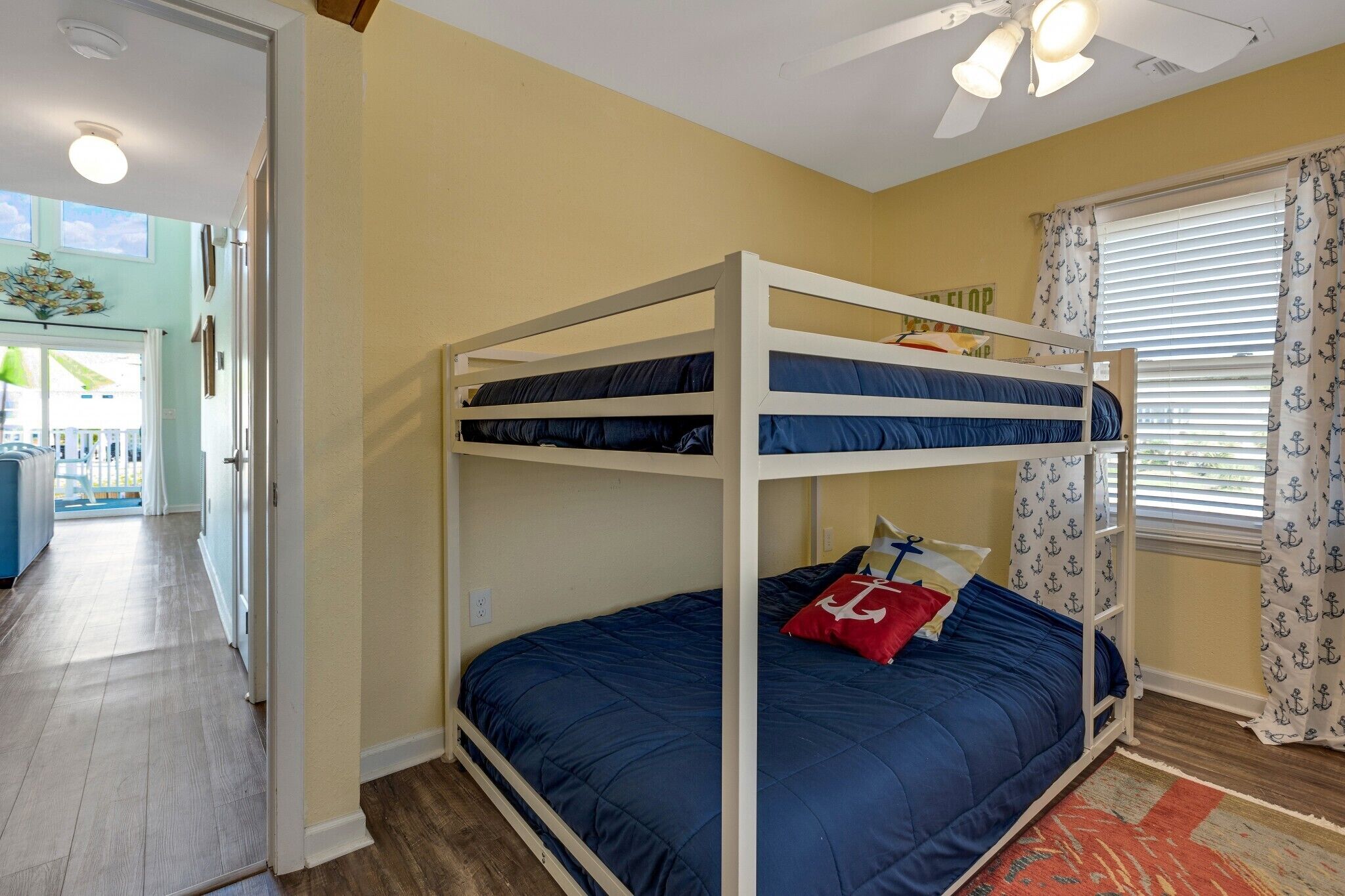 A bunk bed room with a ceiling fan, a window with curtains, and a view of a balcony.