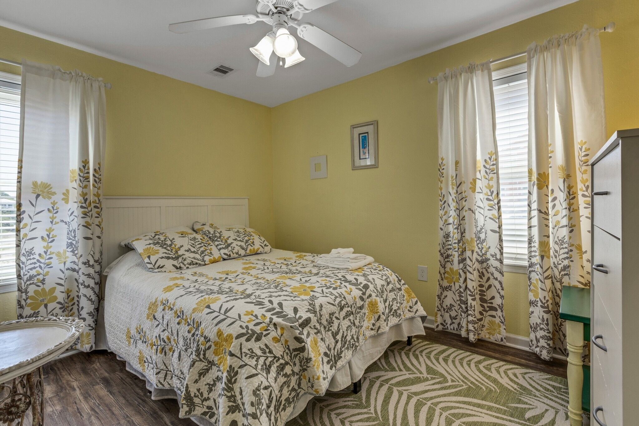 Un dormitorio con cama, cortinas, ventilador de techo y cómoda.
