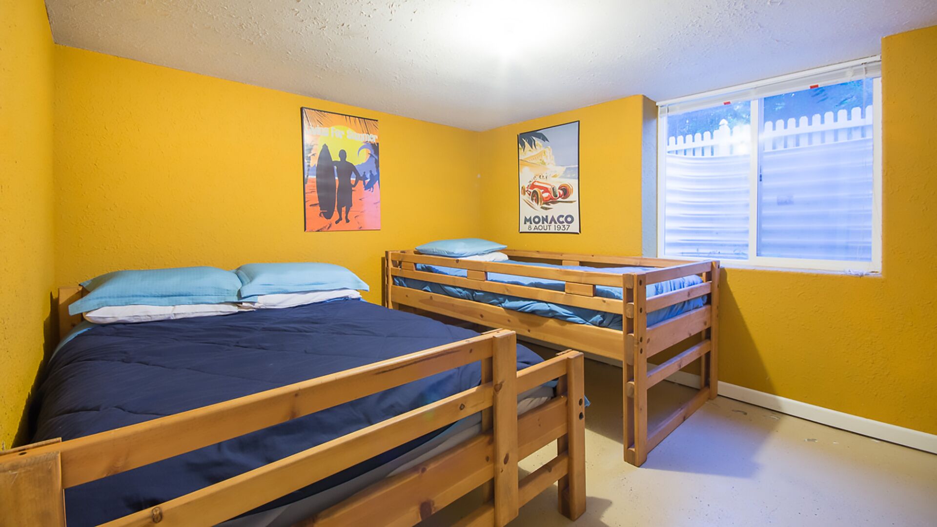 A room with two wooden bunk beds, a window with blinds, and two posters on the wall.