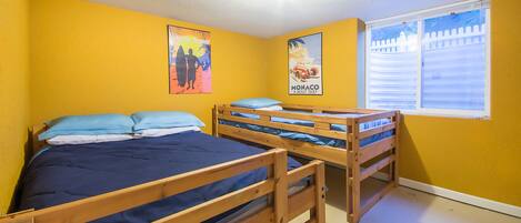 A room with two wooden bunk beds, a window with blinds, and two posters on the wall.