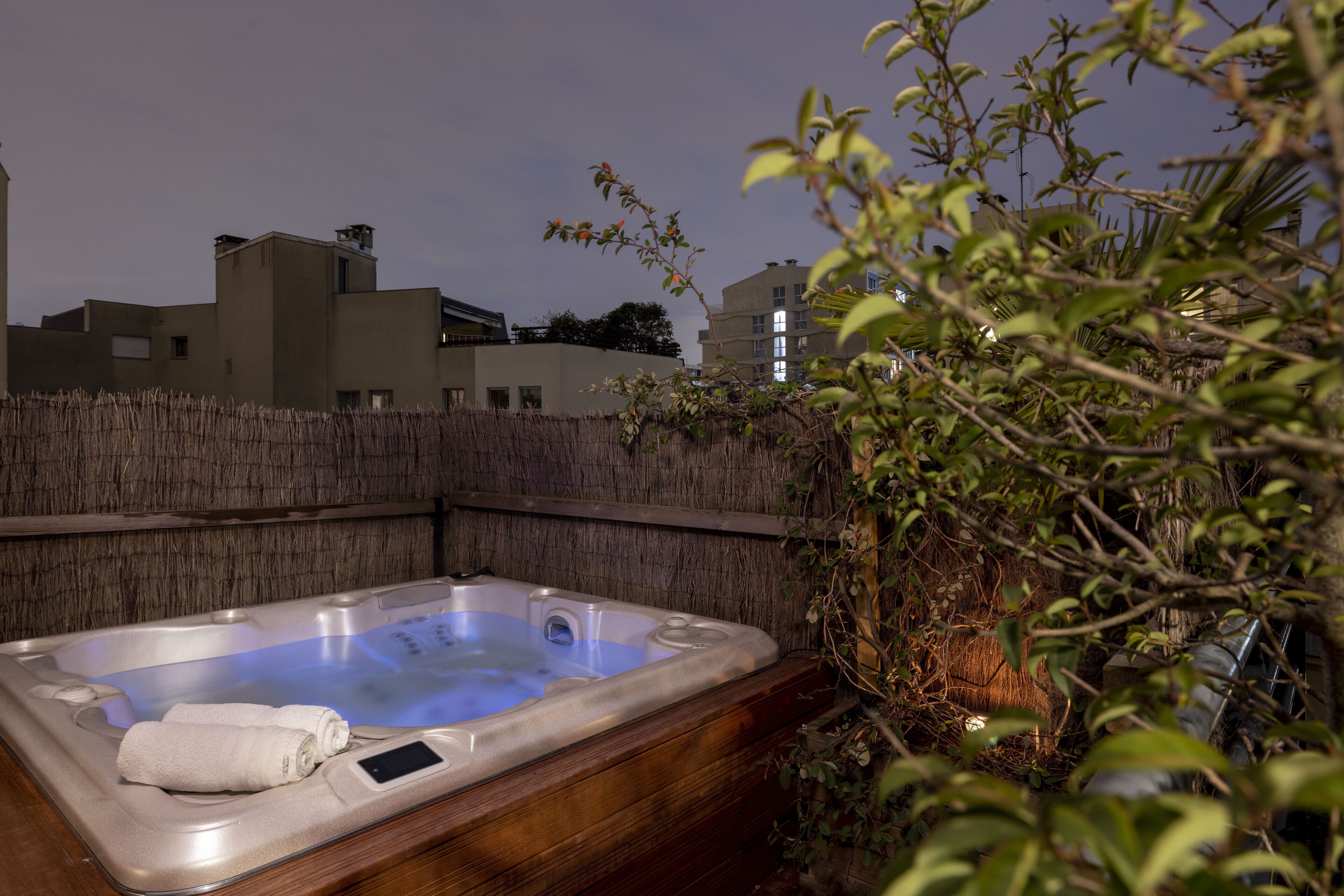 Un bain à remous entouré de bois, une serviette et une clôture en bois en arrière-plan.