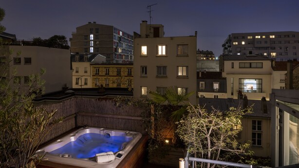 A rooftop with a hot tub, surrounded by buildings and some greenery.