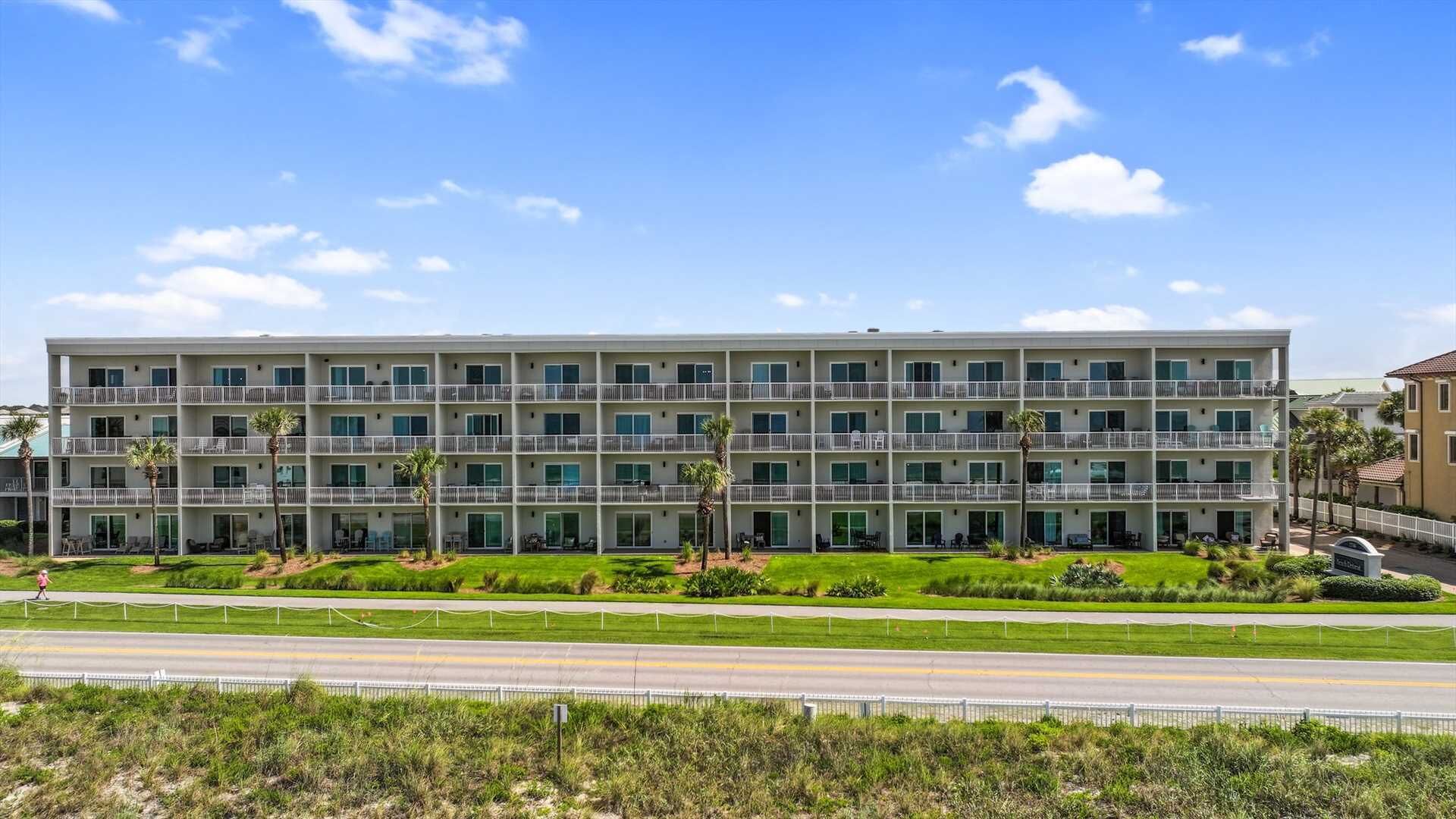 A multi-story hotel with a modern design, featuring balconies, a well-maintained lawn, and a clear sky.
